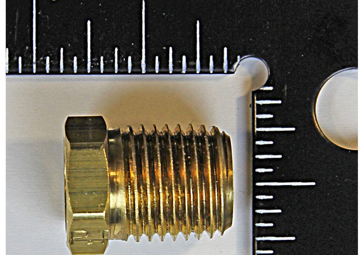 Brass threaded plug with ruler for scale.
